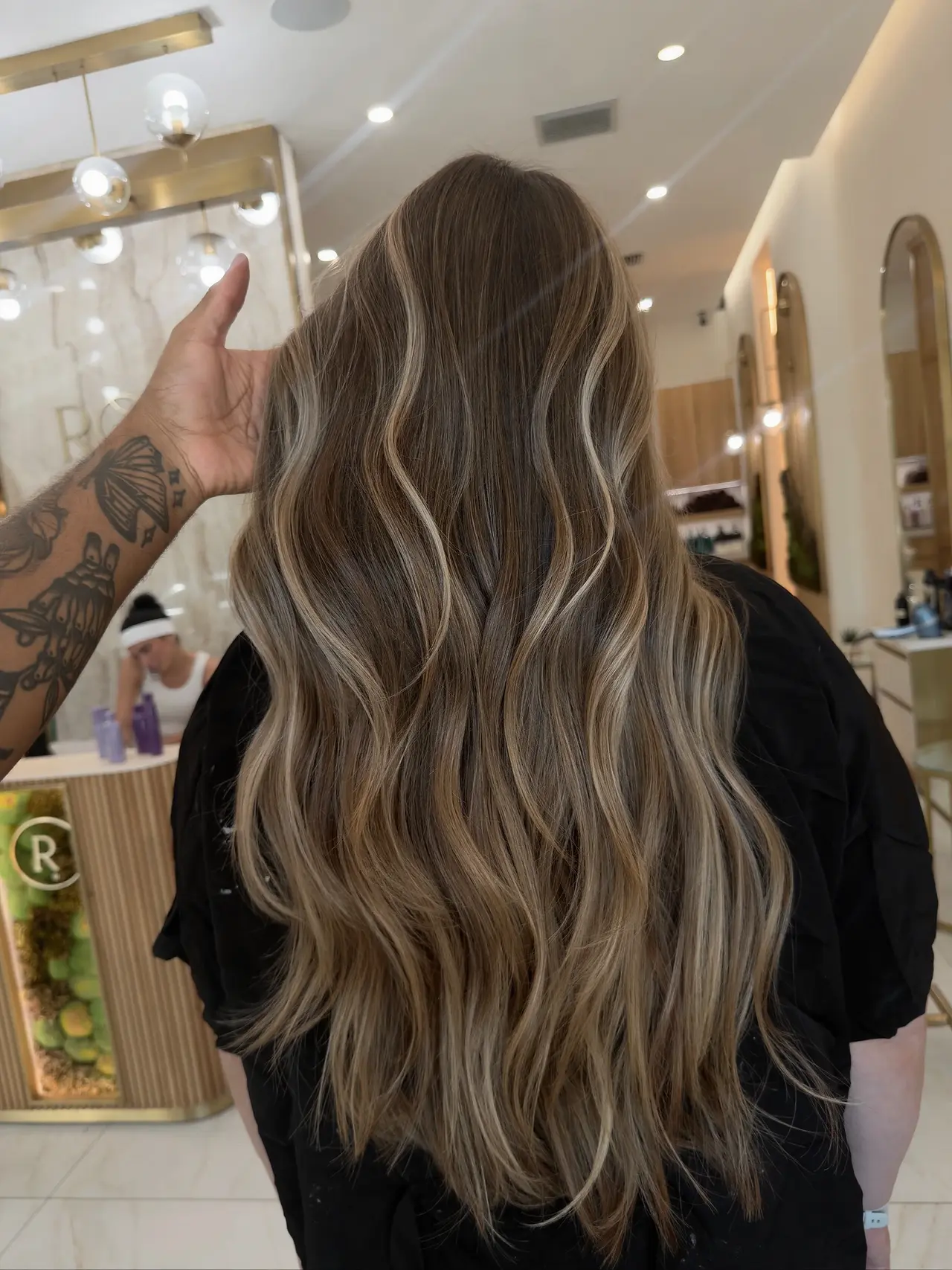 Long brunette waves with subtle lighter ribbons, held by a stylist at Rové