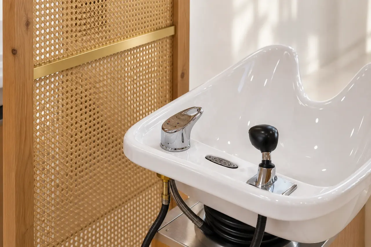 An empty white shampoo basin beside the oak and cane screen at Rové