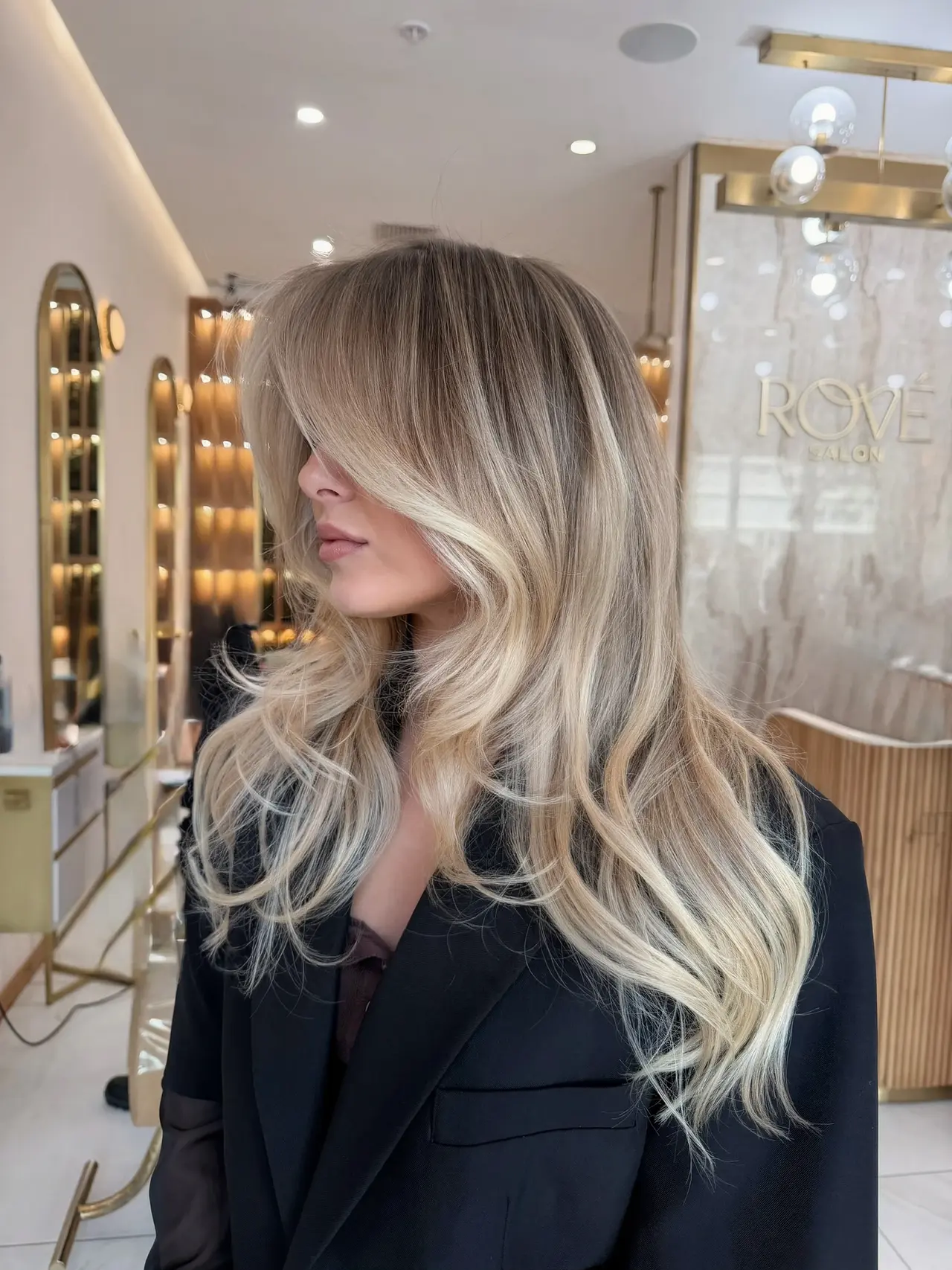 A side view of long blonde layers with a soft face-framing fringe at Rové