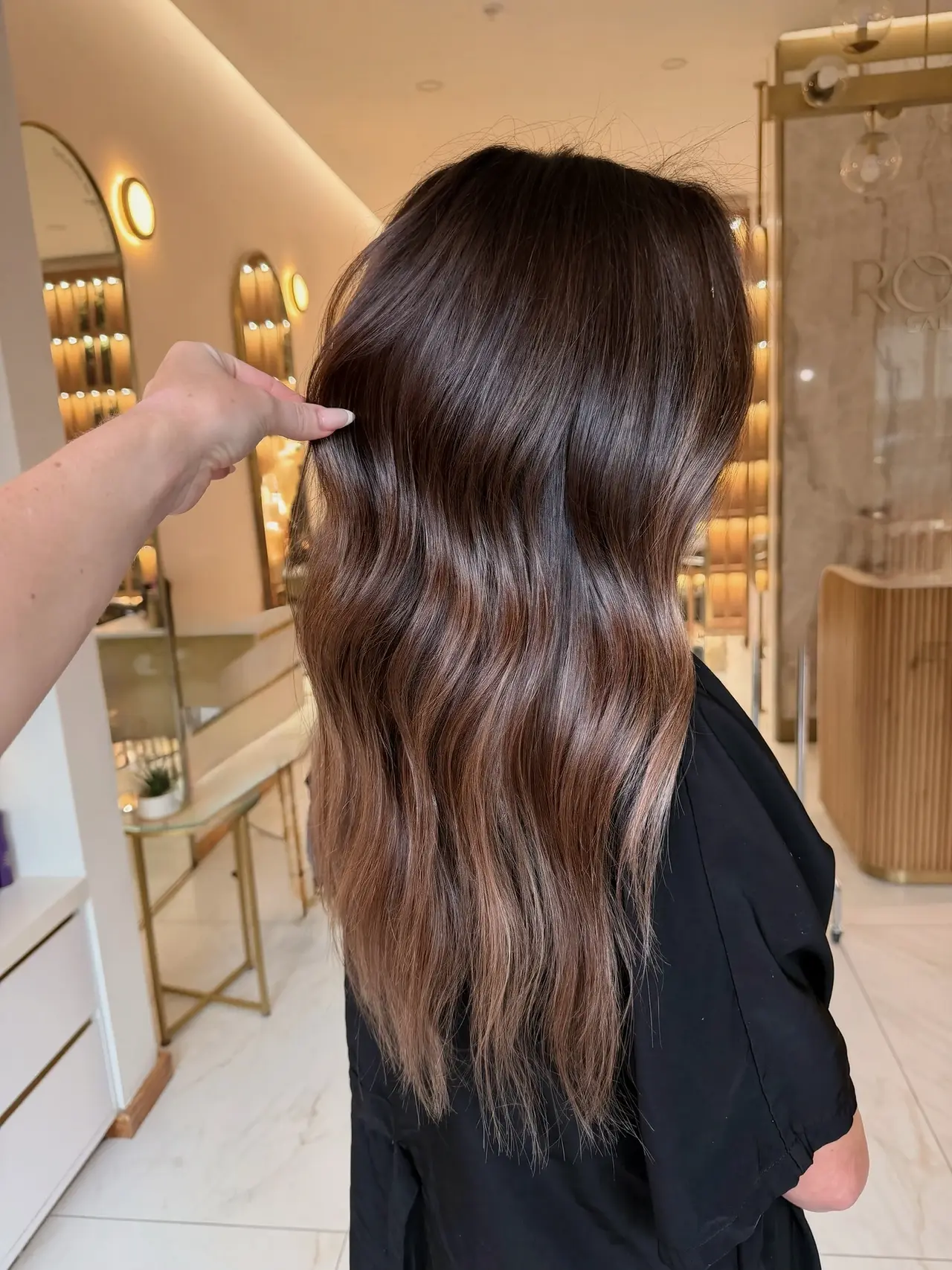 A stylist lifting glossy brunette waves to show their movement at Rové