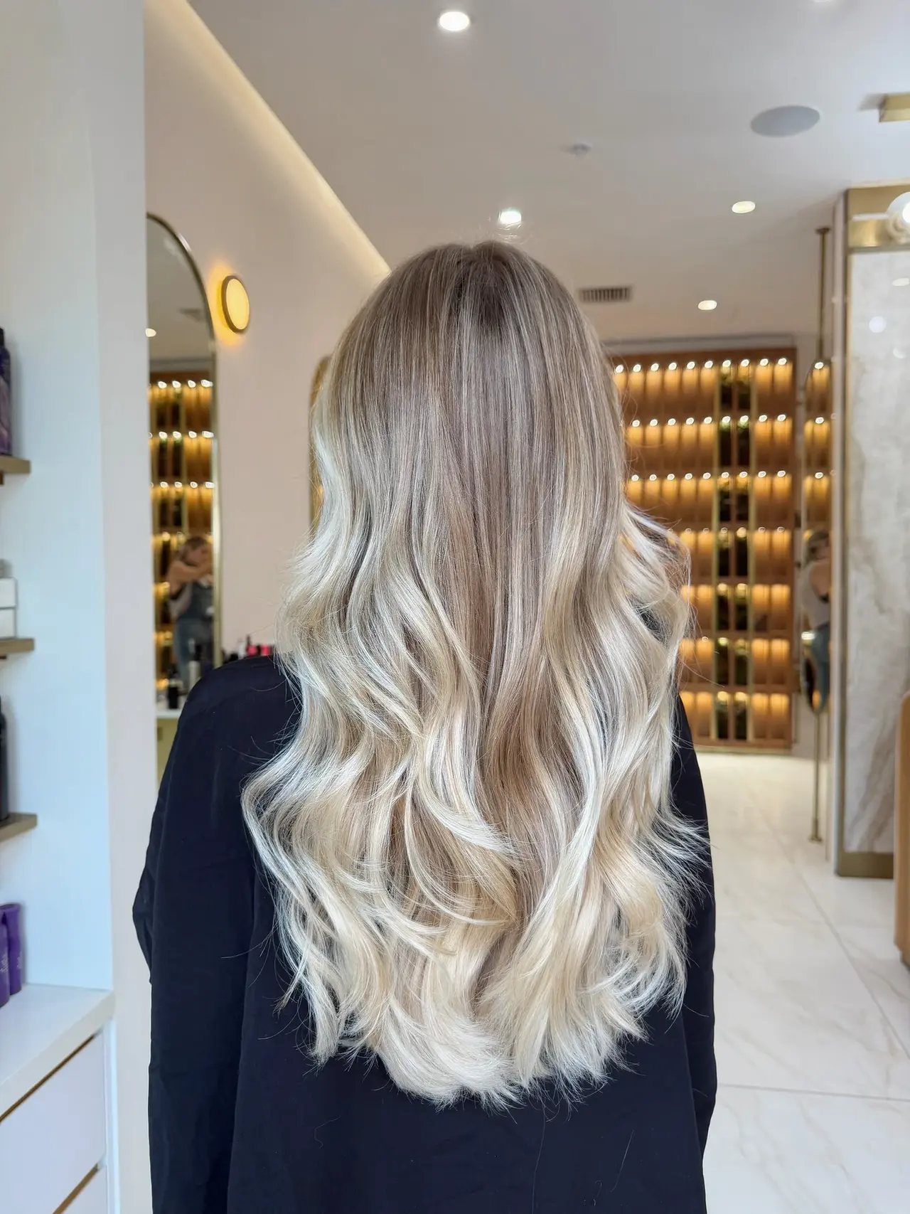 Long softly waved blonde hair with dimensional roots, seen from behind at Rové