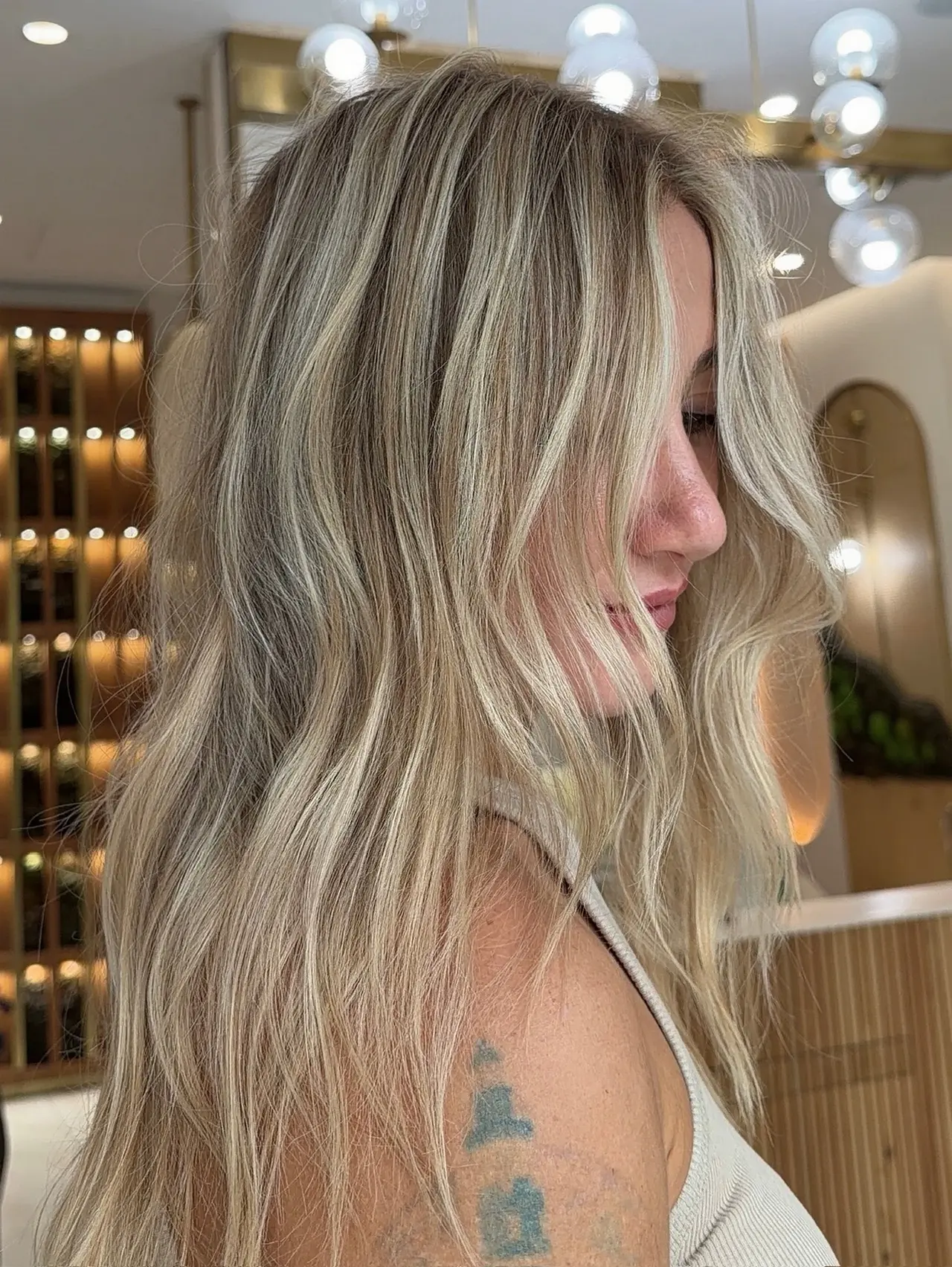 A close side portrait of softly waved blonde hair with dimensional highlights at Rové