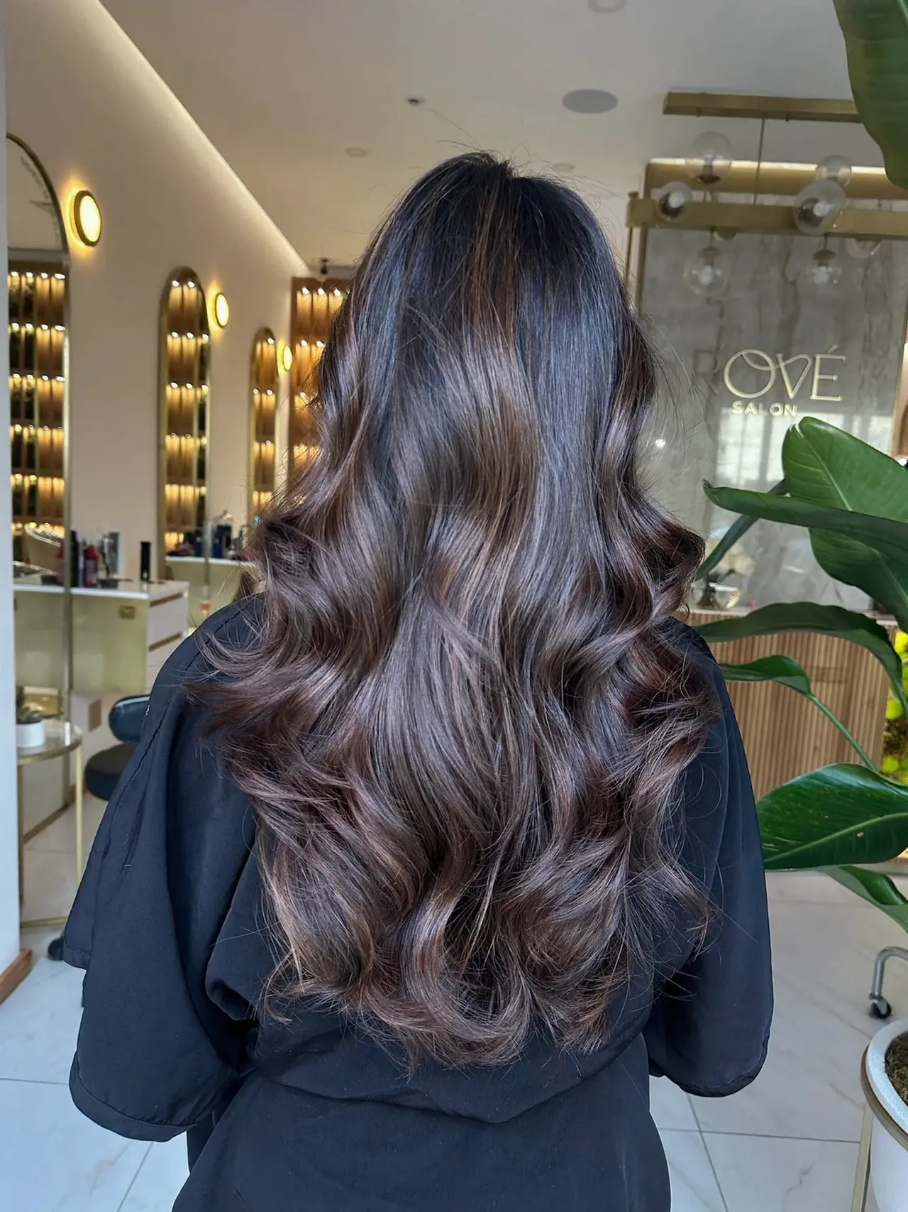 A back view of long glossy brunette hair styled in broad flowing waves at Rové