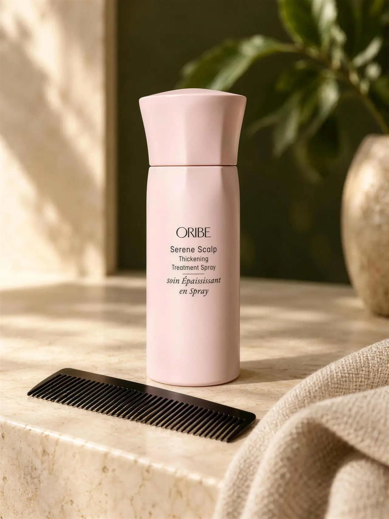 Pink Oribe Serene Scalp treatment bottle with a black comb and folded linen